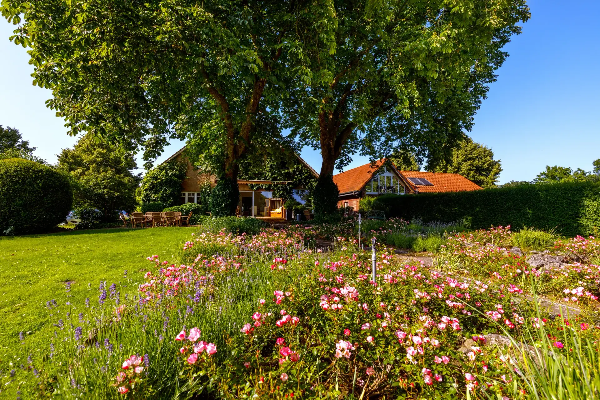 Blumenbeete, Rasen und alte Bäume am Hof